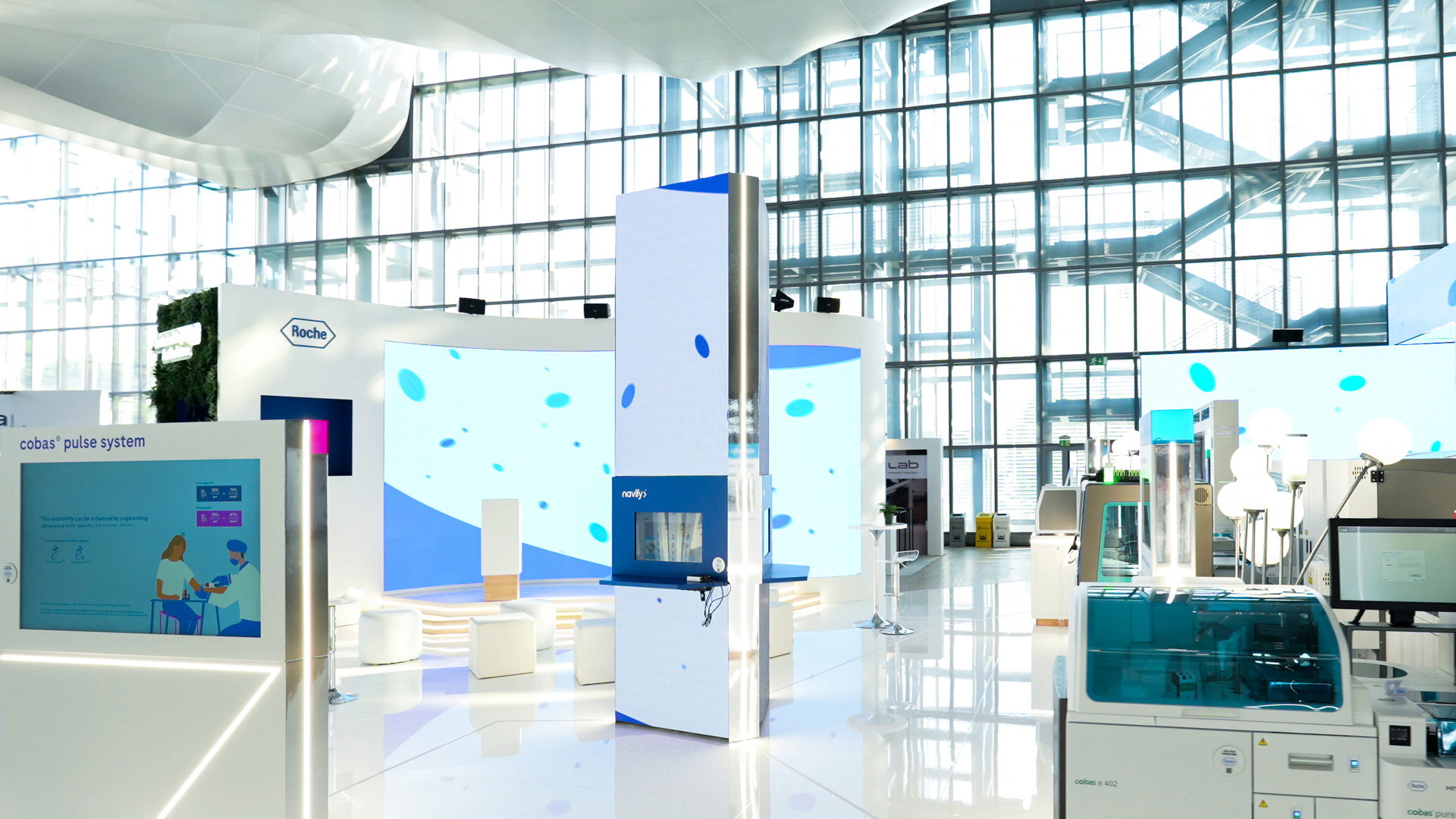Wide view of Roche Diagnostics experiential booth at EML Rome with large digital screens and instrument zones.